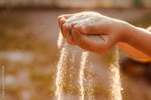 Children's hands release the falling sand. Sand flowing through your hands in the sunset sunlight. photo