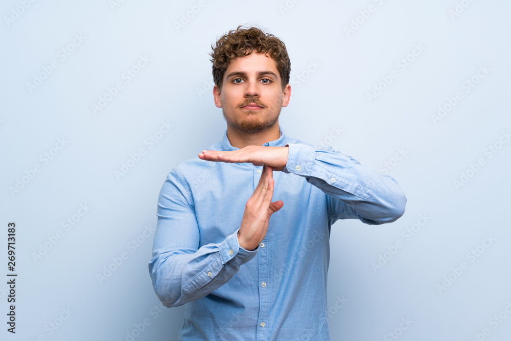 Blonde man over blue wall making time out gesture Blonde man over blue wall making time out gesture