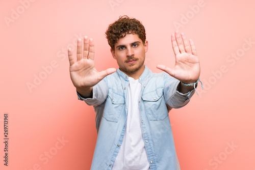 Blonde man over pink wall making stop gesture for disappointed with an opinion © luismolinero