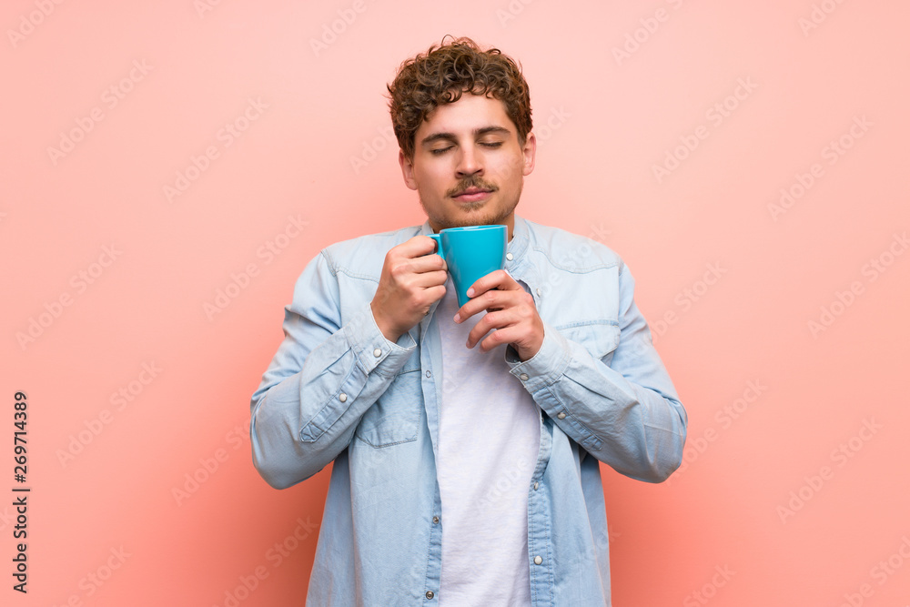Blonde man over pink wall holding a hot cup of coffee Blonde man over pink wall holding a hot cup of coffee