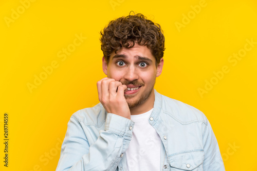 Blonde man over isolated yellow wall nervous and scared