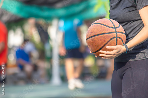 Leather basketball in hand of a woman wearing a watch Background blur tree in park.
