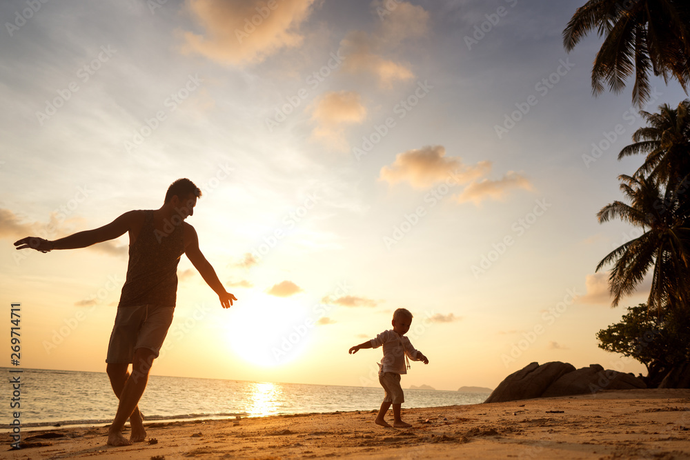 dad and son playing on the sand at the beach at sunset