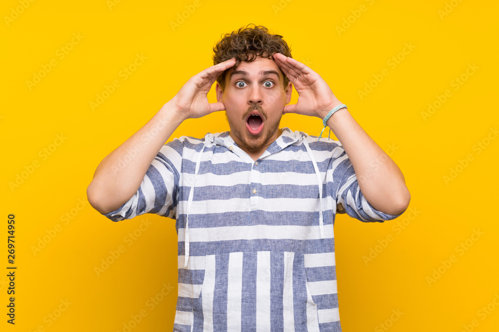 Blonde man over yellow wall with surprise and shocked facial expression Blonde man over yellow wall with surprise and shocked facial expression