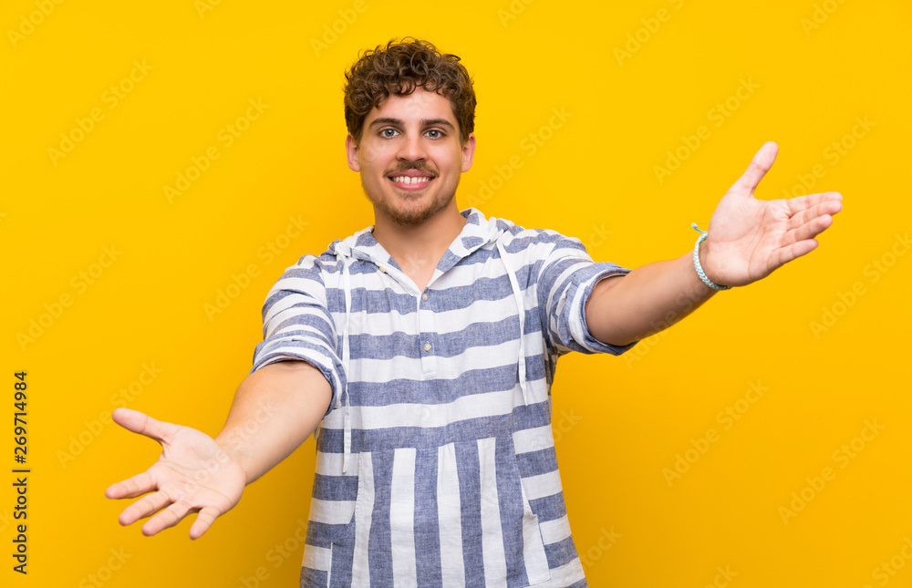 Blonde man over yellow wall presenting and inviting to come with hand Blonde man over yellow wall presenting and inviting to come with hand