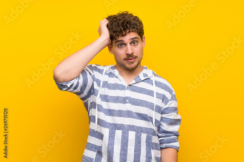 Blonde man over yellow wall with an expression of frustration and not understanding