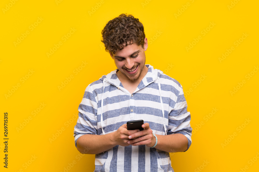 Blonde man over yellow wall sending a message with the mobile Blonde man over yellow wall sending a message with the mobile
