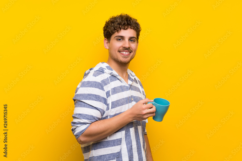 Blonde man over yellow wall holding a hot cup of coffee Blonde man over yellow wall holding a hot cup of coffee