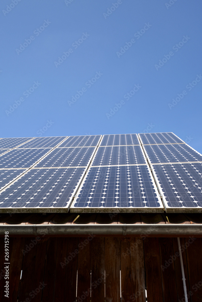modern solar cells or photovoltaic on the roof of an old woodshed with new gutter in front of azure sky, solar panel on blue sky background modern solar cells or photovoltaic on the roof of an old woodshed with new gutter in front of azure sky, solar panel on blue sky background