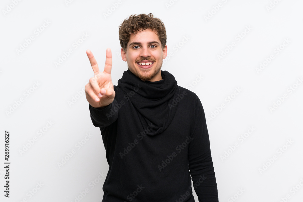 Fototapeta premium Blonde man over isolated white wall smiling and showing victory sign