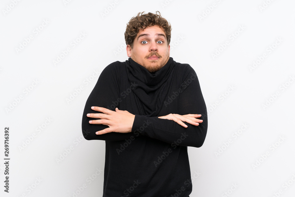 Blonde man over isolated white wall making doubts gesture while lifting the shoulders Blonde man over isolated white wall making doubts gesture while lifting the shoulders