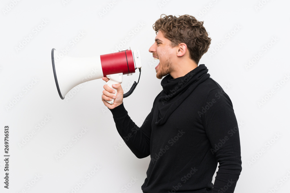 Blonde man over isolated white wall shouting through a megaphone Blonde man over isolated white wall shouting through a megaphone