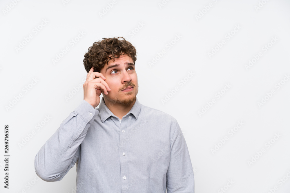 Blonde man over isolated white wall having doubts and with confuse face expression Blonde man over isolated white wall having doubts and with confuse face expression