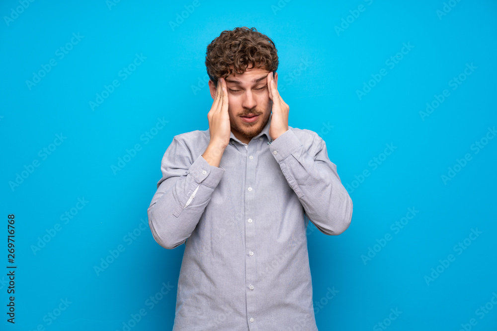 Blonde man over blue wall with headache Blonde man over blue wall with headache