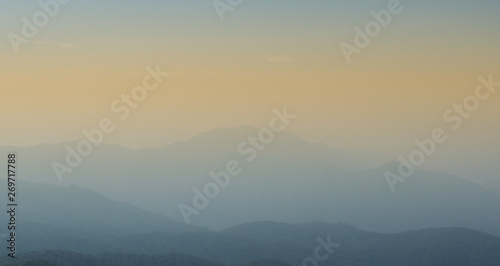 Layers of mountains with orange sunset and foggy