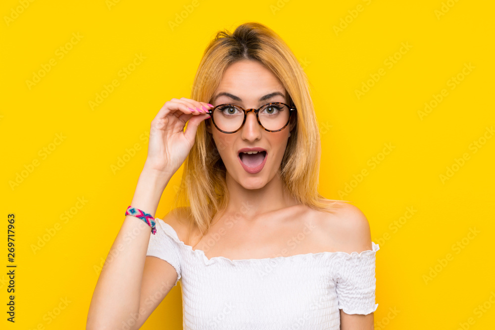 Young blonde woman over isolated yellow wall with glasses Young blonde woman over isolated yellow wall with glasses