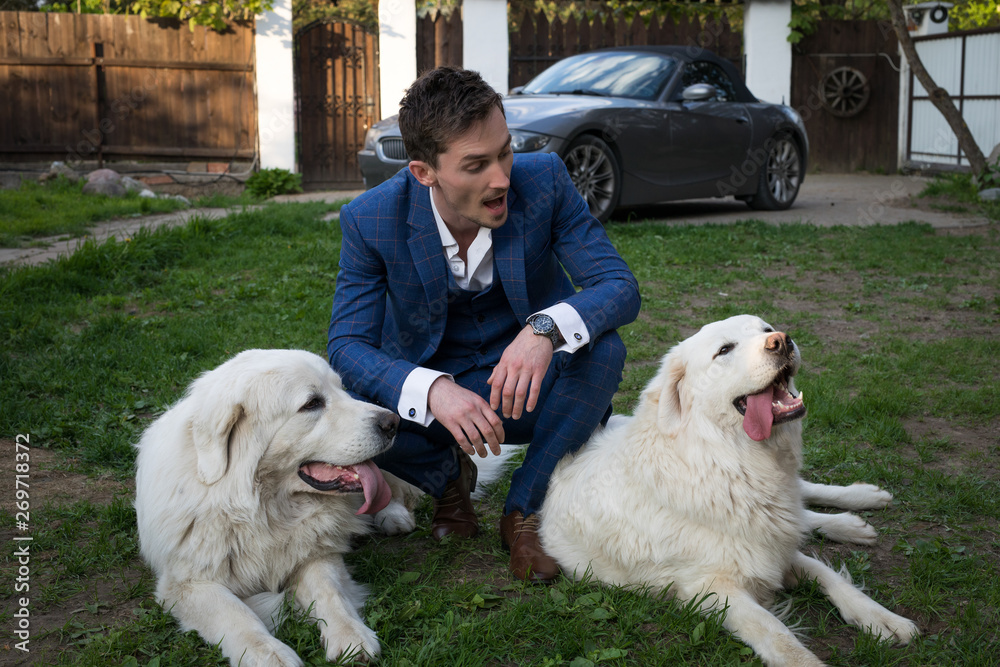 Elegant young handsome man in blue costume play with Tatra Shepherd Dog outdoor. Elegant young handsome man in blue costume play with Tatra Shepherd Dog outdoor.