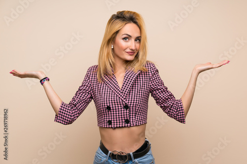 Young blonde woman with pink jacket over isolated wall making doubts gesture
