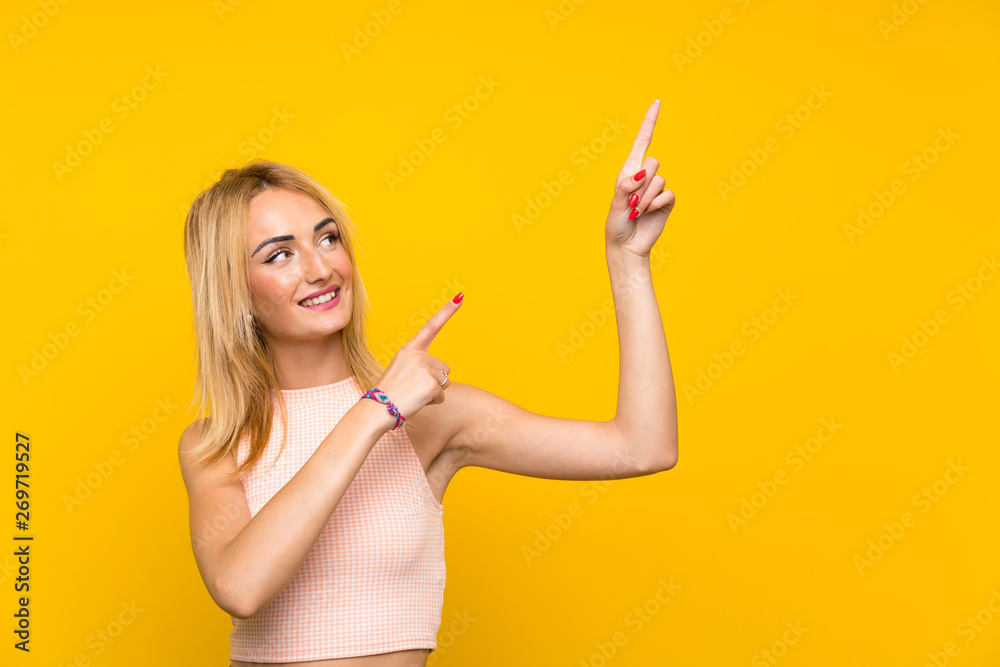 Young blonde woman over isolated yellow wall pointing with the index finger a great idea Young blonde woman over isolated yellow wall pointing with the index finger a great idea