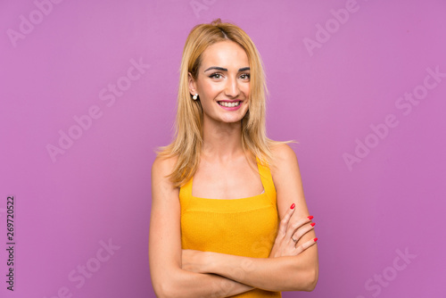 Young blonde woman over purple background laughing