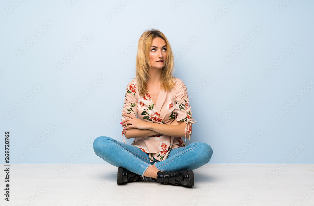 Young blonde woman sitting on the floor with confuse face expression Young blonde woman sitting on the floor with confuse face expression