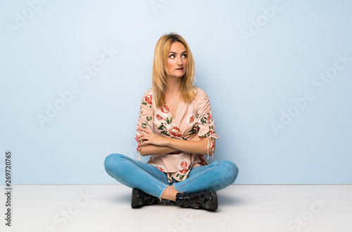 Young blonde woman sitting on the floor with confuse face expression
