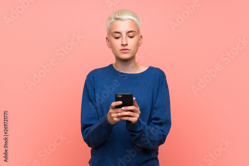 Teenager girl with white short hair over pink wall sending a message with the mobile