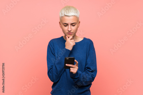 Teenager girl with white short hair over pink wall thinking and sending a message © luismolinero
