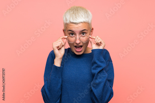 Teenager girl with white short hair over pink wall with glasses and surprised