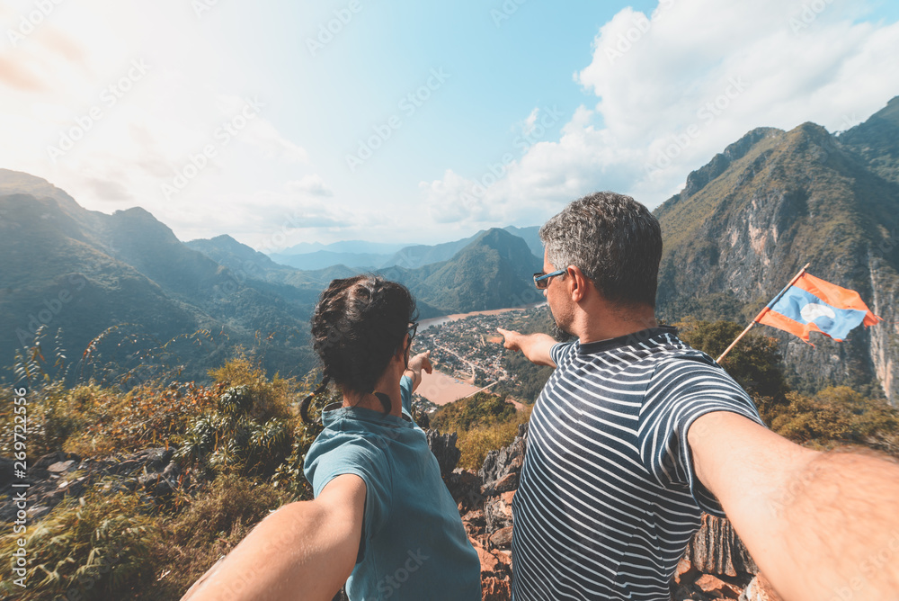 Couple selfie on mountain top at Nong Khiaw panoramic view over Nam Ou River valley Laos  travel destination in South East Asia, mature people traveling millenials concept, teal orange toned