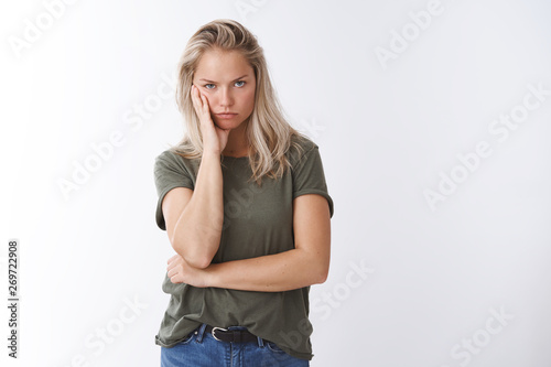 Annoyed woman cannot stand hearing lies leaning head on arm looking from under forehead irritated and intense with dismay and disrespect standing bothered and pressured over white background