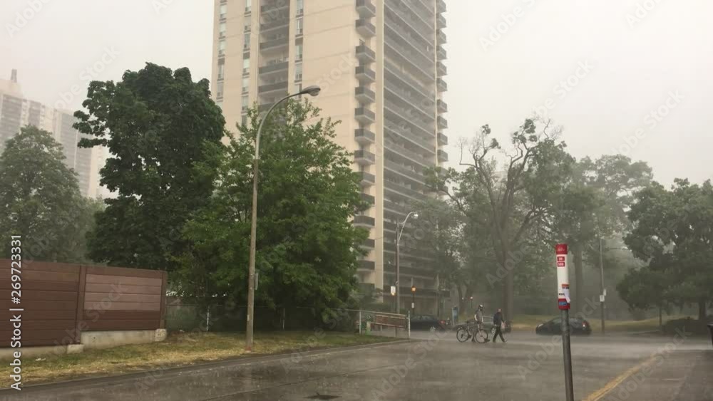 Torrential rainfall in an urban area, with people crossing the road holding a bike. Torrential rainfall in an urban area, with people crossing the road holding a bike.