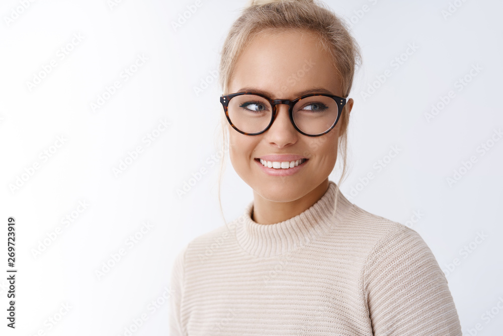 Charming young female in sweater and black frames turning right and smiling posing for journalists attending interview standing pleased and happy against white background, grinning carefree