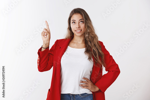 Cute dreamy young 25s millennial curly-haired female wearing red jacket looking pointing up smiling curiously amused, high-hopes cheering up self-encouraging before important job interview