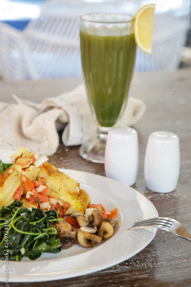 Spanish potato tortilla served with mushrooms, spinach and green detox drink on the wooden table, casual dining restaurant food Spanish potato tortilla served with mushrooms, spinach and green detox drink on the wooden table, casual dining restaurant food