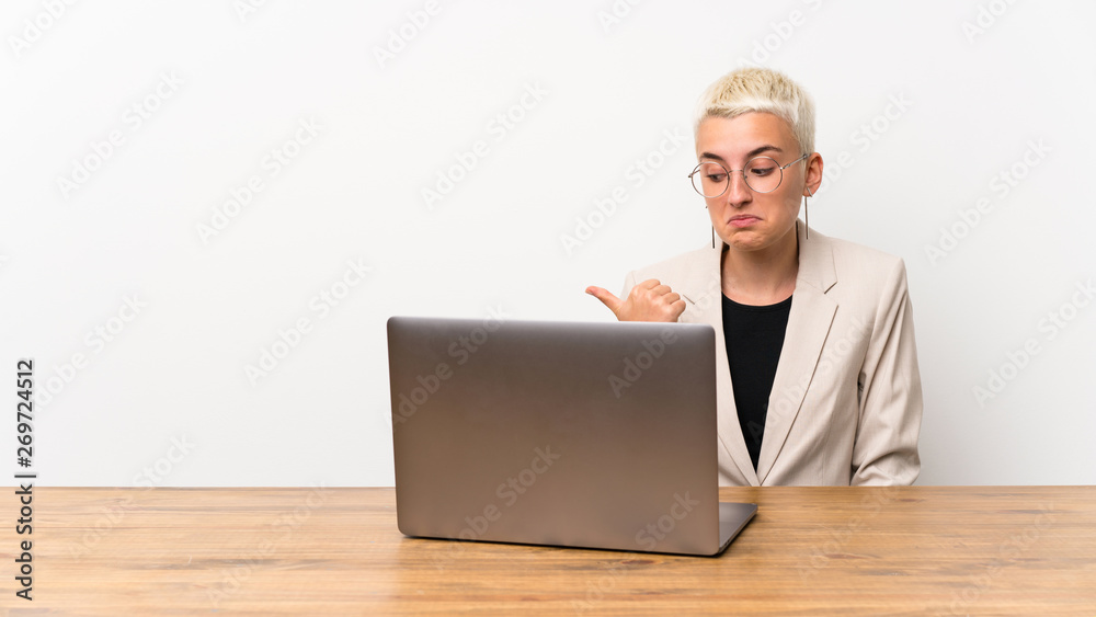 Teenager girl with short hair with a laptop unhappy and pointing to the side Teenager girl with short hair with a laptop unhappy and pointing to the side