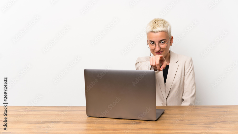 Teenager girl with short hair with a laptop points finger at you with a confident expression Teenager girl with short hair with a laptop points finger at you with a confident expression