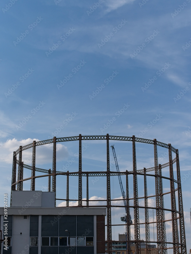 Silhouette of an old gasholder at sunset against blue sky with white clouds in East London, UK.