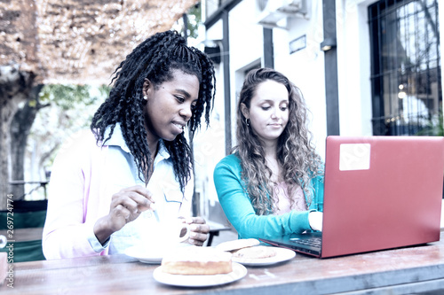 Working meeting between two young women in front of a café, with laptop and mobile