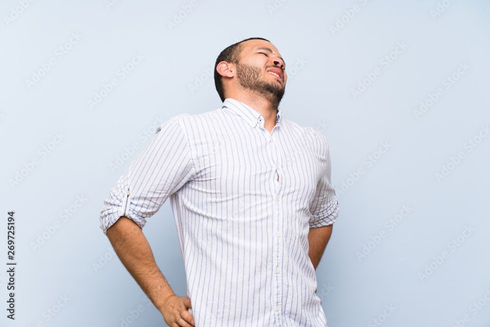 Colombian man over isolated blue wall suffering from backache for having made an effort Colombian man over isolated blue wall suffering from backache for having made an effort