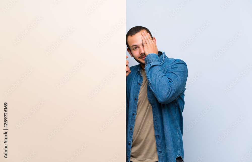 Colombian man holding an empty placard covering a eye by hand Colombian man holding an empty placard covering a eye by hand
