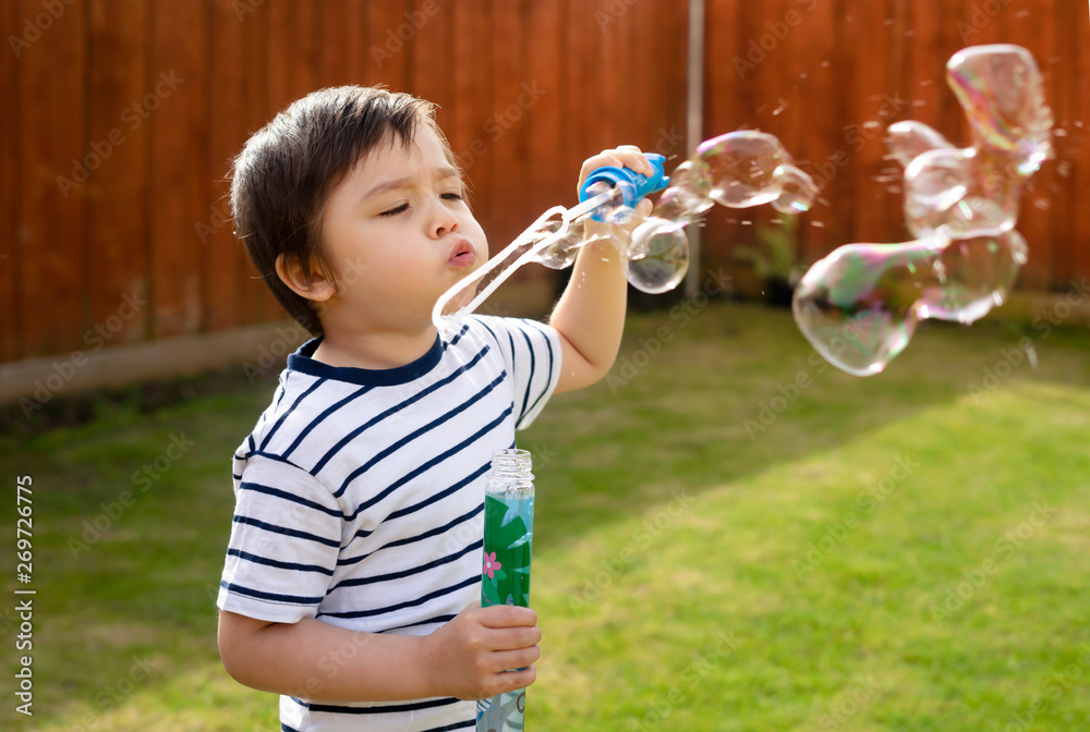 Happy boy blowing soap bubbles in the garden, Cute 4 years old kid blowing bubble wand with a funny face, Active kid playing in the garden on a sunny summer day, Out doors activities for children Happy boy blowing soap bubbles in the garden, Cute 4 years old kid blowing bubble wand with a funny face, Active kid playing in the garden on a sunny summer day, Out doors activities for children