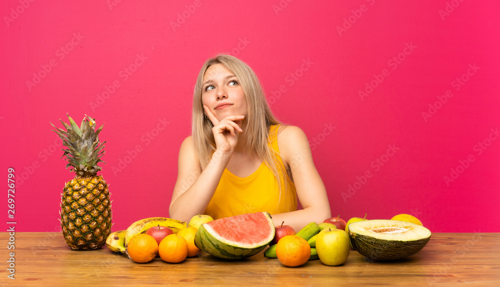 Young blonde woman with lots of fruits thinking an idea Young blonde woman with lots of fruits thinking an idea