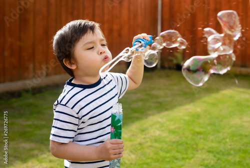 Happy boy blowing soap bubbles in the garden, Cute 4 years old kid blowing bubble wand with a funny face, Active kid playing in the garden on a sunny summer day, Out doors activities for children