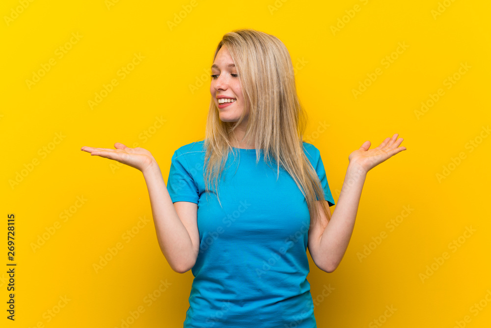 Young blonde woman over isolated yellow background holding copyspace with two hands Young blonde woman over isolated yellow background holding copyspace with two hands