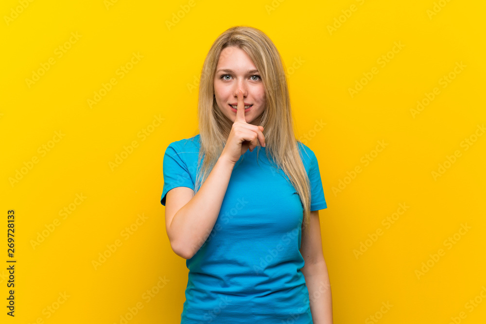 Young blonde woman over isolated yellow background showing a sign of silence gesture putting finger in mouth Young blonde woman over isolated yellow background showing a sign of silence gesture putting finger in mouth