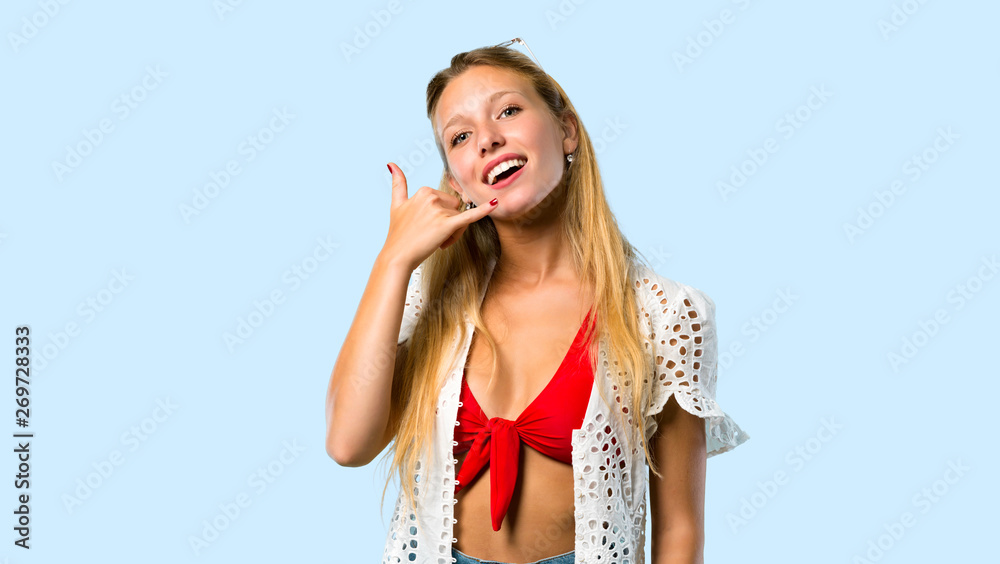 Fototapeta premium Blonde girl in summer vacation making phone gesture. Call me back sign on blue background