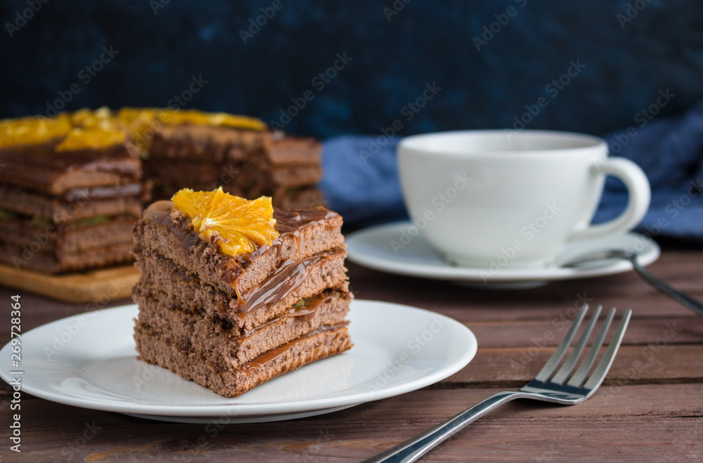 piece of chocolate cake decorated with orange slice on plate cup of tea on wooden table soft focus piece of chocolate cake decorated with orange slice on plate cup of tea on wooden table soft focus