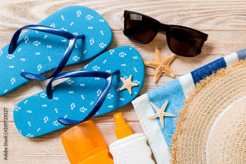 flip flops, straw hat, starfish, sunscreen bottle, body lotion spray on wooden background top view . flat lay summer beach sea accessories background, holiday concept
