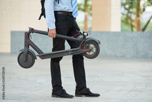 Close-up of businessman holding electric scooter in his hand while standing outdoors in the city